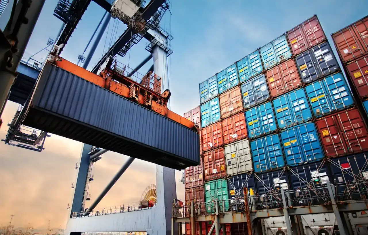 Crane lifting a shipping container beside stacked containers on a ship