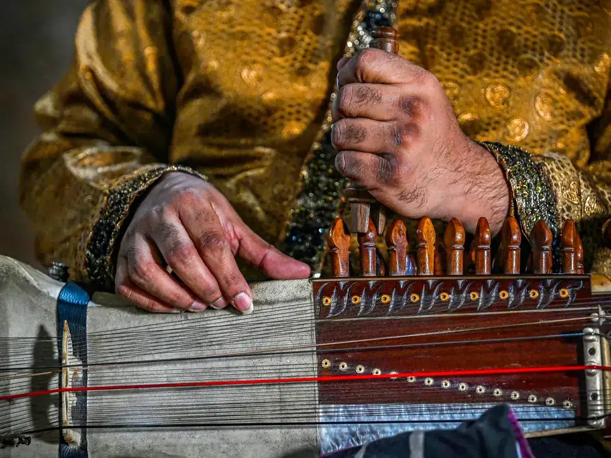 Musician playing a handmade sarangi with carved wooden pegs